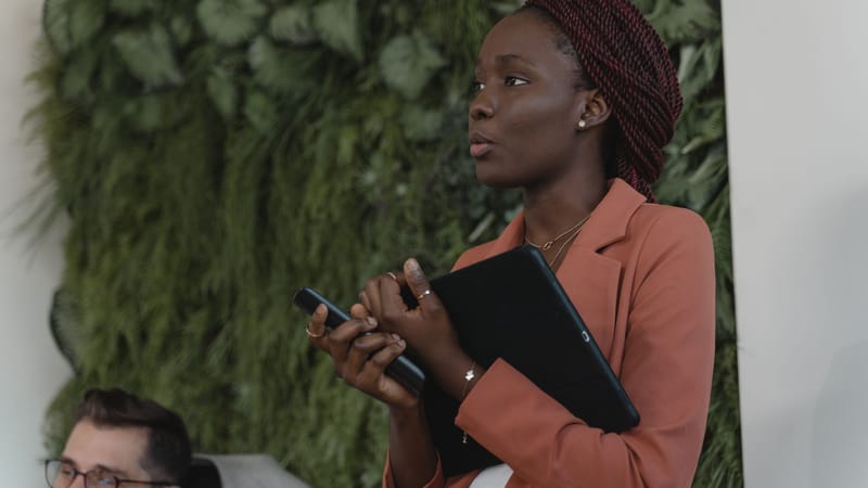 Femme d'affaires confiante tient une tablette tout en parlant dans un cadre de bureau moderne.
