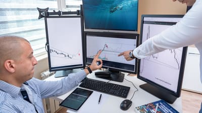 Deux professionnels du secteur analysent des données financières sur plusieurs écrans d'ordinateur dans un cadre de bureau.