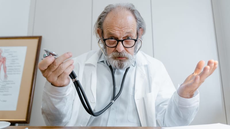 Un médecin senior gesticulant avec un stéthoscope dans un cadre clinique, soulignant la télémédecine.