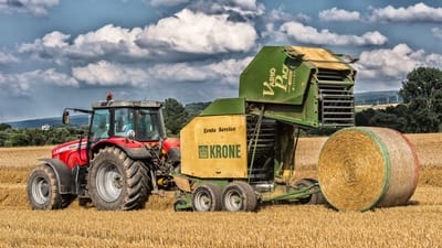 Scène rurale d'un tracteur rouge et d'une presse à balles dans un champ de Höxter, récoltant du foin sous un ciel nuageux.
