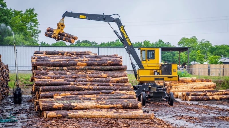Un manipulateur de matériaux jaunes soulevant des billots dans une scierie, mettant en avant des machines industrielles modernes en action.