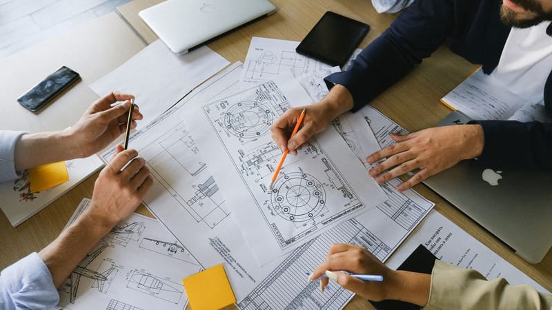 Équipe d'ingénierie engagée dans une réunion collaborative, examinant des plans techniques dans un environnement de bureau.