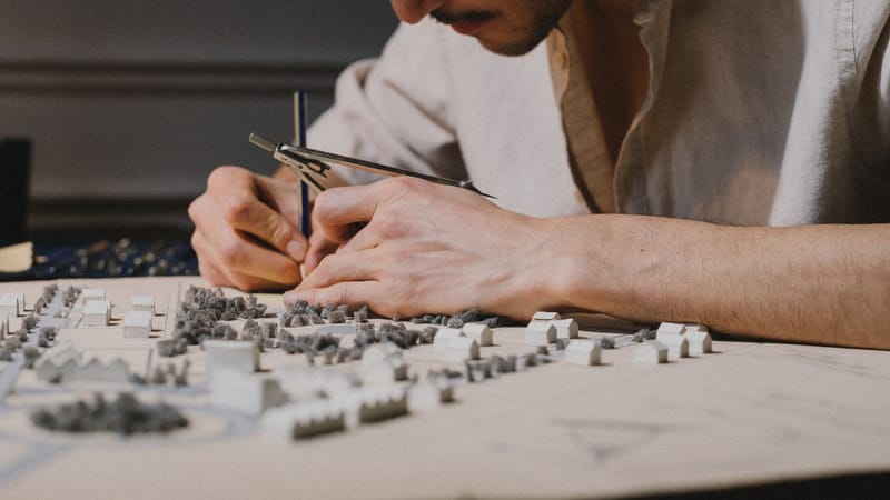 Architecte concentré sur la création d'un modèle détaillé à l'aide d'un compas à l'intérieur, mettant en avant la précision et la créativité.
