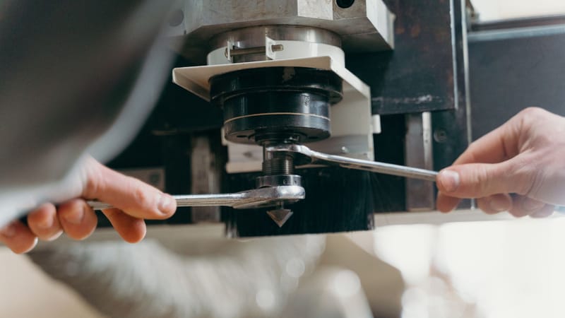 Gros plan des mains ajustant une machine CNC à l'aide de clés dans un environnement industriel.