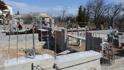 Chantier ensoleillé avec des travailleurs sur une fondation en béton sous un ciel bleu clair.