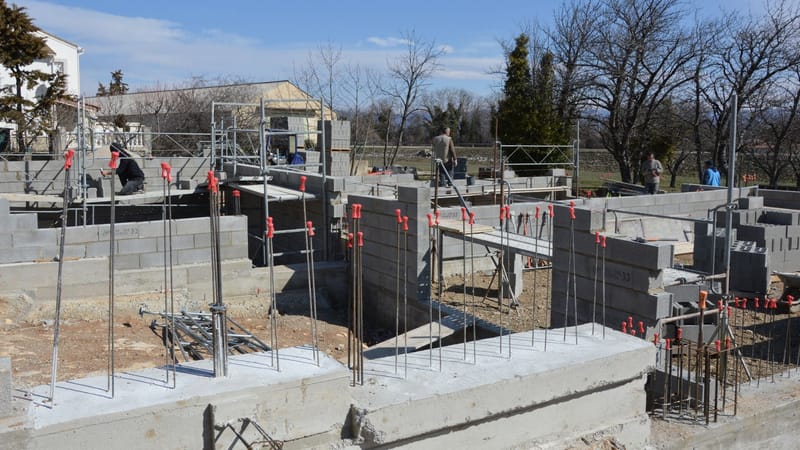 Chantier ensoleillé avec des travailleurs sur une fondation en béton sous un ciel bleu clair.
