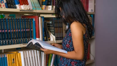 Jeune femme lisant un livre dans une bibliothèque à Delhi, Inde, entourée d'étagères de livres sur l'économie d'entreprise.