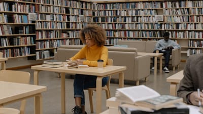 Étudiants étudiant dans une bibliothèque universitaire entourée d'étagères et de tables.
