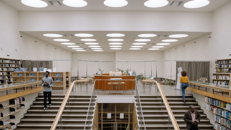 Intérieur spacieux de bibliothèque avec un design moderne, des étagères et des personnes dans les escaliers.