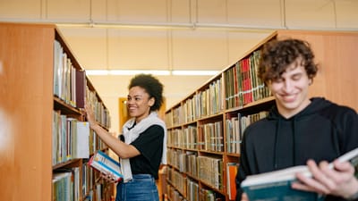 Deux étudiants étudiant dans une bibliothèque universitaire, choisissant des livres parmi les étagères.