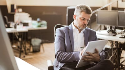 Homme d'affaires en tenue formelle écrivant sur un carnet avec concentration dans un bureau moderne.