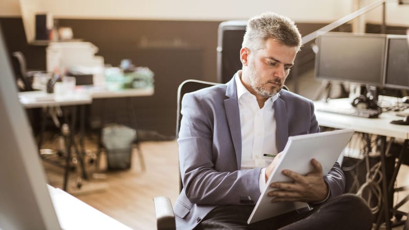 Homme d'affaires en tenue formelle écrivant sur un carnet avec concentration dans un bureau moderne.