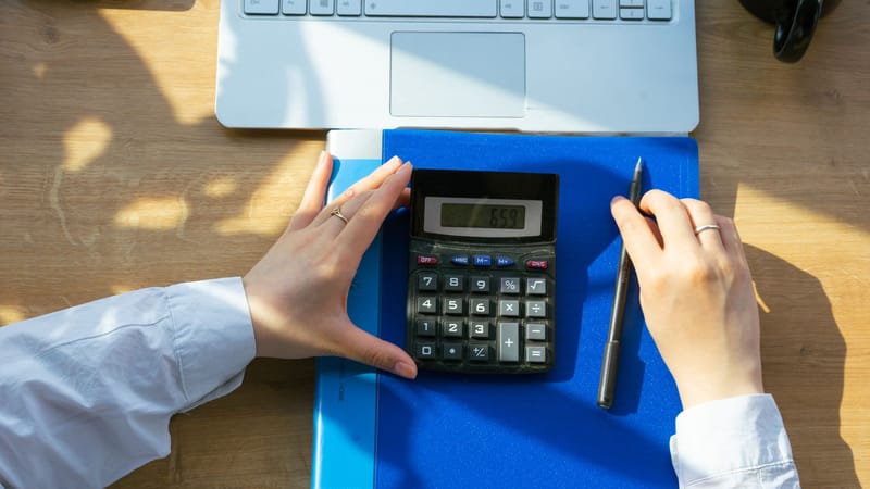 Mains utilisant une calculatrice sur un bureau avec un ordinateur portable, un stylo et un carnet. Parfait pour des thèmes de bureau ou de finances.