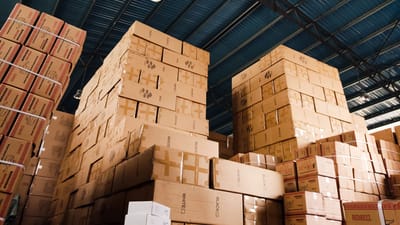 Hautes piles de boîtes en carton organisées dans un entrepôt avec un plafond métallique bleu.