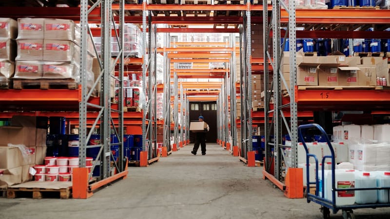 Un travailleur portant une boîte dans une allée de stockage d'entrepôt bien organisée.